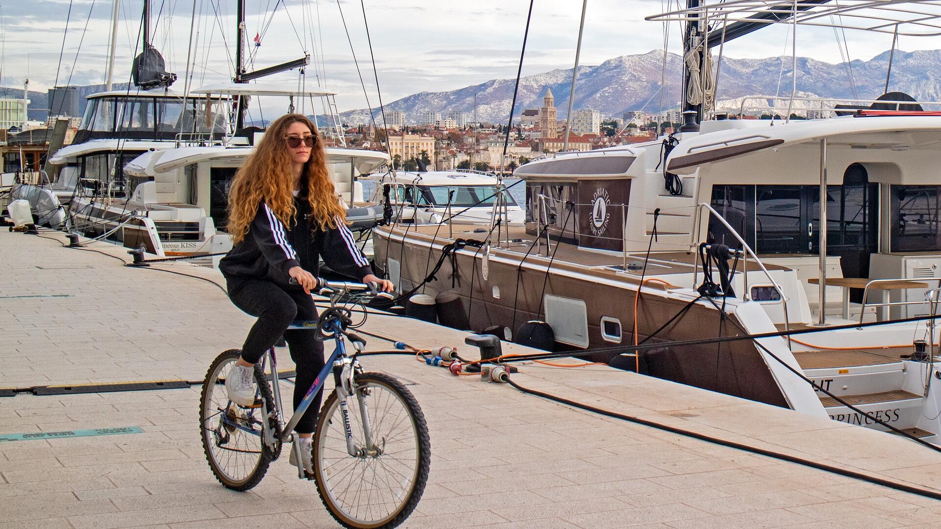 A-girl-biking-passed-Lagoon-catamarans-in-Split-starting-point-of-Bike-and-sail-cruise-in-Croatia